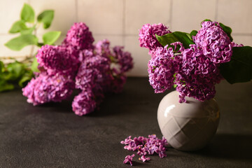 Vase with bouquet of beautiful lilac flowers on dark table near light wall, closeup