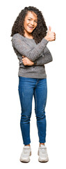 Young beautiful woman with curly hair wearing grey sweater Looking proud, smiling doing thumbs up gesture to the side