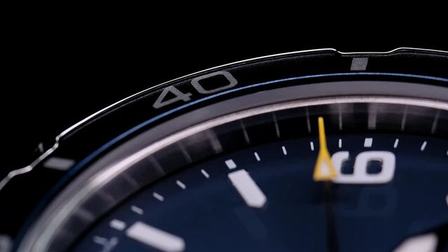 Extreme closeup of yellow second arrow passing by on blue clock face. Lengthwise view of luxury swiss watch. Closeup real time shot. Running second arrow