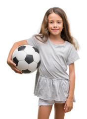 Brunette hispanic girl holding soccer football ball with a happy face standing and smiling with a...