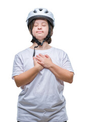 Young adult cyclist woman with down syndrome wearing safety helmet over isolated background smiling with hands on chest with closed eyes and grateful gesture on face. Health concept.