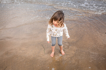 upper view of little girl with brown hair walking along the sea coast on sand