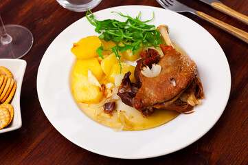 Confit de canard, roasted tasty duck confit with stew potatoes and arugula on a ceramic plate