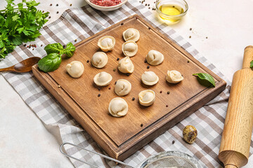 Fototapeta na wymiar Board with uncooked dumplings on light background
