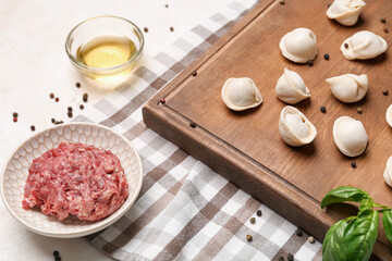 Board with uncooked dumplings and ingredients on light background