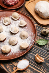 Plate with uncooked dumplings on wooden background