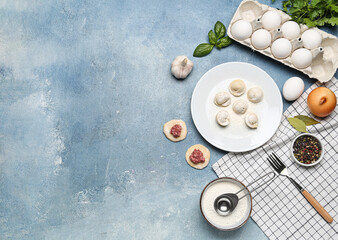 Fototapeta na wymiar Plate with uncooked dumplings and ingredients on blue background
