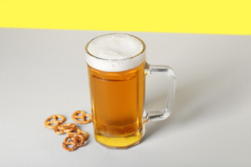 Mug of cold beer and pretzels on color background, closeup