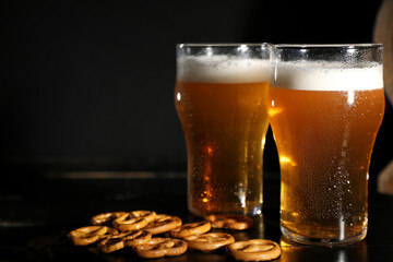 Glasses of cold beer with pretzels on dark background, closeup