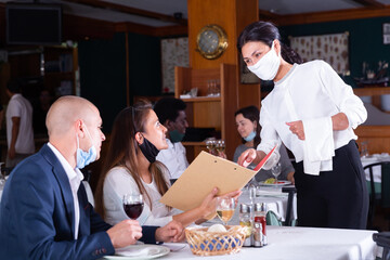 smiling female waiter taking order from couple in restaurante diring virus