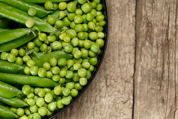 Fresh green peas in pods and peeled green peas in a round plate on a wooden background, top view, copy space.