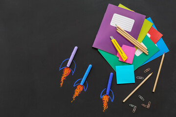 Creative composition with drawn rockets and different stationery on black chalkboard