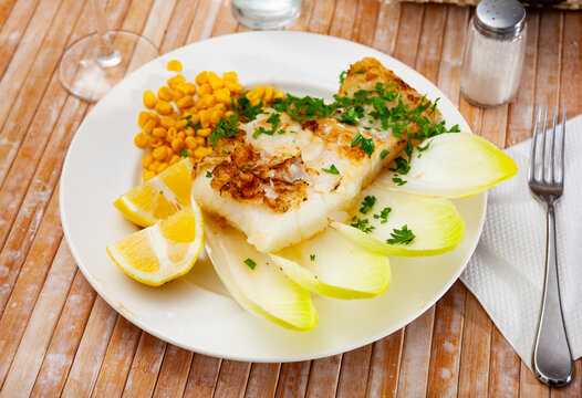 Delicious fried cod fillet with endive, corn, and greens at the plate