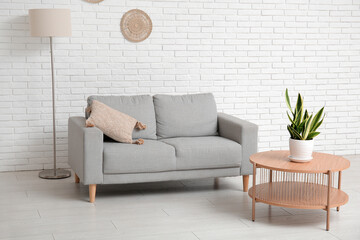 Interior of living room with sofa, table and houseplant near white brick wall