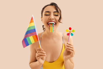 Young woman in swimsuit with candies and LGBT flag on beige background