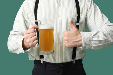 Young man in traditional German clothes with beer showing thumb-up on green background, closeup