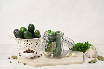Jar and colander with fresh cucumbers for preservation on table