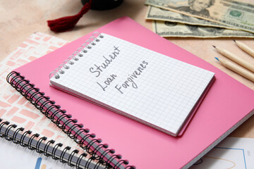 Notebook with text STUDENT LOAN FORGIVENESS, and dollar banknotes on beige table