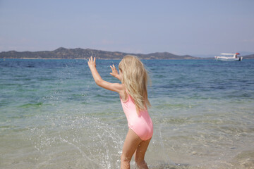 Naklejka premium Adorable little girl in pink swimsuit splashing water at the beach. Idyllic summer vacation concept.