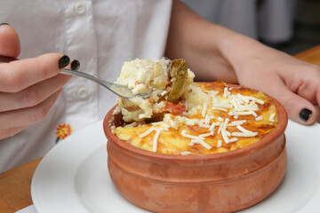 Woman eating traditional greek moussaka prepared in clay pot	
