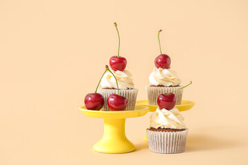 Stands with tasty cherry cupcakes on beige background