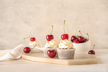 Board with tasty cherry cupcakes on light background
