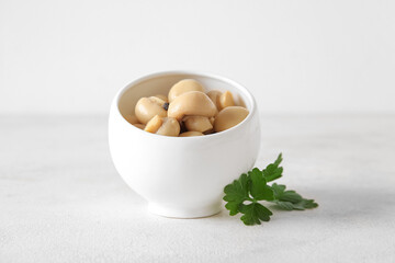 Bowl with canned mushrooms on light background