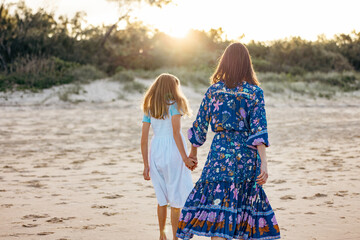 Rear view of mother and daughter walking on the beach at sunset. Family vacation on the Gold Coast