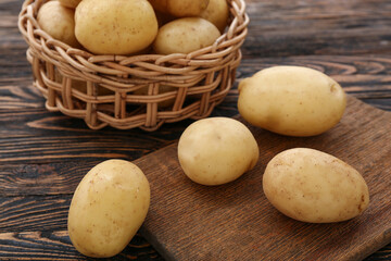 Fototapeta na wymiar Wicker bowl and board with raw potatoes on wooden background