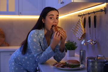 Young woman eating sandwich in kitchen at night. Bad habit
