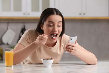 Woman using smartphone while having breakfast at table in kitchen. Internet addiction