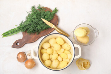 Pot and bowl with peeled potatoes on light background