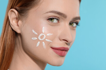 Beautiful young woman with sun protection cream on her face against light blue background, closeup....