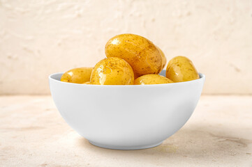 Bowl with raw potatoes on light background