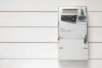 Electricity meter on white wooden wall, space for text