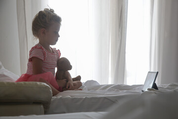 Child sitting on bed watching cartoons on digital tablet	