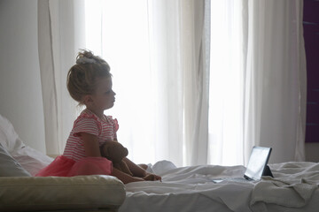 Child sitting on bed watching cartoons on digital tablet	