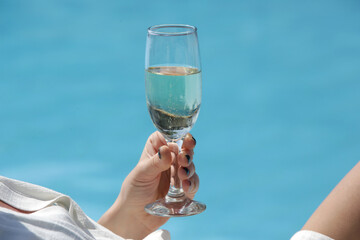 Woman enjoying hot day, having a glass of prosecco at the pooside. Relaxing summer vacation concept.	