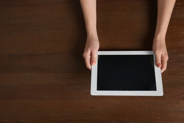 Woman working with tablet at wooden table, top view. Space for text