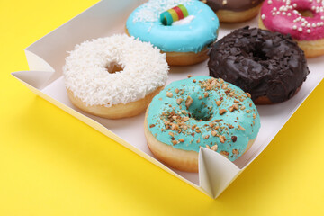 Box with tasty glazed donuts on yellow background, closeup