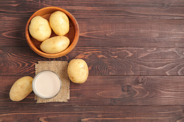 Glass of tasty potato milk and fresh vegetables on wooden background