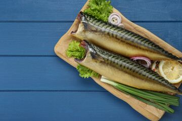 Delicious smoked mackerels and products on blue wooden table, top view. Space for text