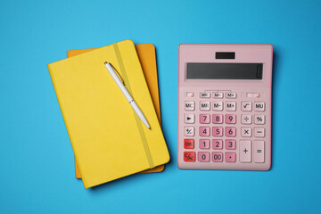 Calculator, notebooks and pen on light blue background, flat lay