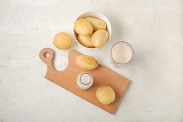 Bottle and glass of tasty potato milk with fresh vegetables on light background