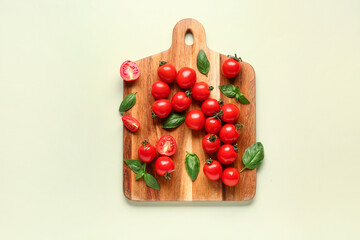 Wooden board with fresh cherry tomatoes and basil on light green background