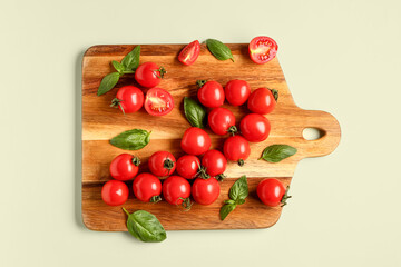 Wooden board with fresh cherry tomatoes and basil on light green background