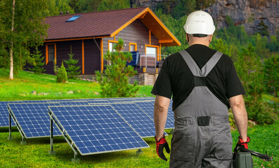 Engineer near solar panels. Photovoltaic battery in front cottage. Man electrician with back to...