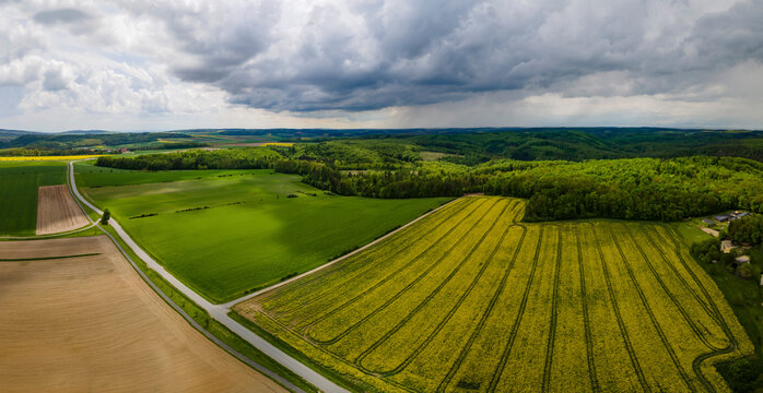 Aerial drone panoramic view of the forest quarter in Lower Austria with canola fields in the foreground and forest in the background under a storm and cloud covered sky.