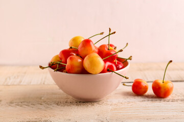 Bowl with sweet yellow cherries on white wooden table
