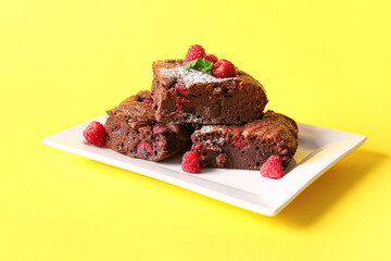 Plate with pieces of raspberry chocolate brownie on yellow background